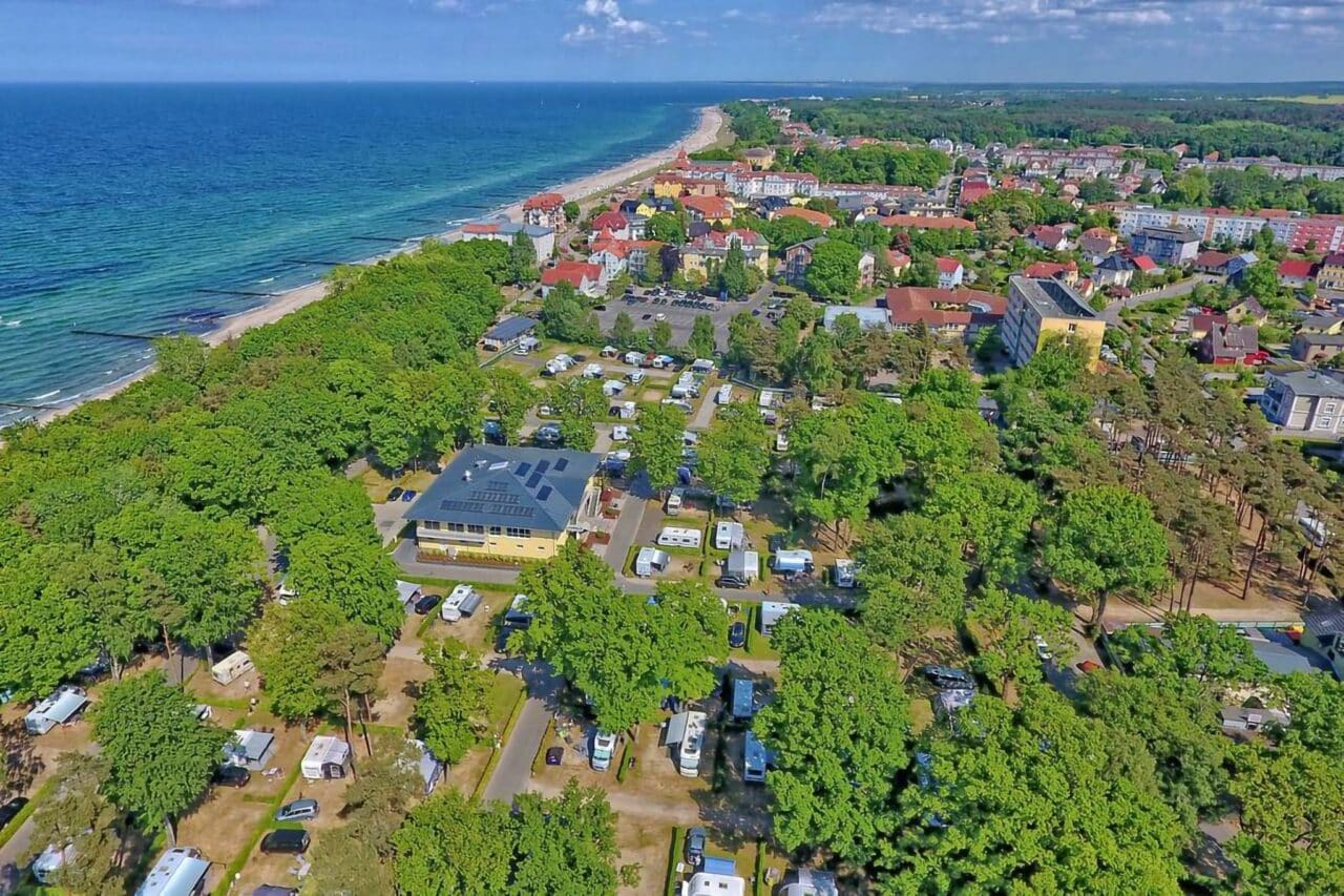 Les paradis des campeurs : Les meilleurs campings d'Allemagne, à voir absolument 1 Camping.info n°1 en Allemagne : Camping Kühlungsborn. On peut voir une vue aérienne d'un camping dans la verdure, avec la mer en arrière-plan.